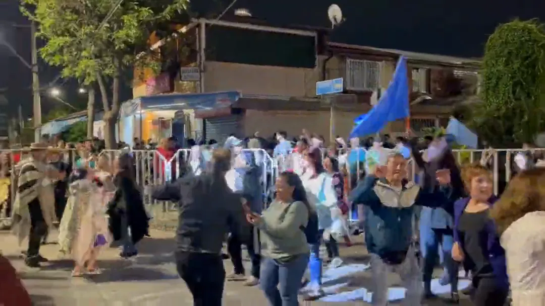 Público celebrando con banderas en la calle frente al escenario, al atardecer